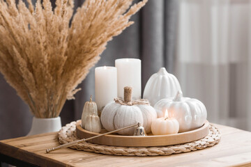 Still-life. Knitted pumpkin,  pumpkin-shaped candles and white ceramic pumpkins on a wooden tray on a coffee table in the home interior of the living room. Cozy autumn concept.