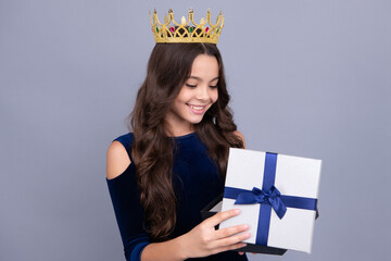 Child with gift present box on isolated background. Presents for birthday, Valentines day, New Year or Christmas. Happy face of princess in crown, positive and smiling emotions of teenager girl.