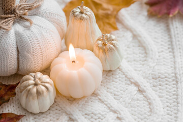 Fototapeta na wymiar Still-life. Knitted pumpkin, autumn leaves, white knitted plaid and a burning candle in the shape of a pumpkin. Cozy autumn concept.