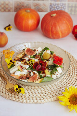 Vegetarian salad with feta, edible flowers, figs, peach, basil on ceramic tile background with sunflowers and pumpkin decorations.