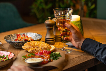 a glass of white wine in a man's hand against the background of a laid table in a restaurant