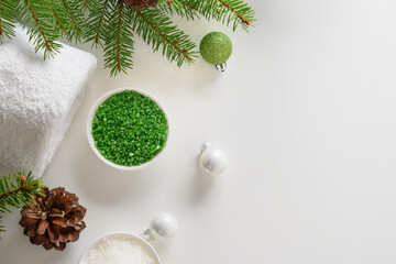 Obraz na płótnie Canvas Winter body skin care and Christmas Spa concept and preparation before holiday. Cosmetic sea salt , baubles, evergreen fir branches on white background. View from above. Special offer for beauty