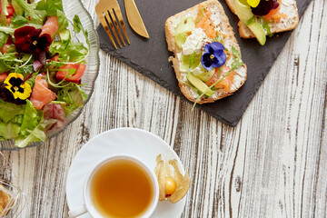 Healthy pescetarian breakfast - toasts and fresh salad. Appetizer with salmon, cottage cheese, edible flowers, avocado and greens. Tea cup. Atmospheric autumn lunch time