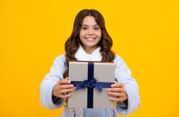 Portrait of a teenager child girl holding present box isolated over yellow studio background. Present, greeting and gifting concept. Birthday holiday concept.