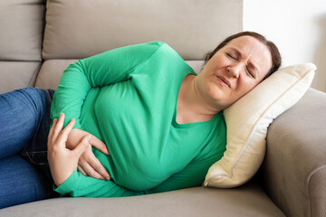 Woman experiencing stomach pain while lying on the sofa at home
