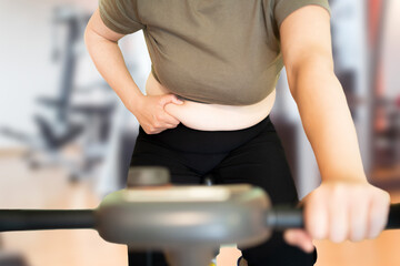 Shot of a young woman exercising at the gym on a stationary bike and measuring her fats