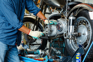 Fototapeta premium Bike maintenance and repair. Mechanic man fixing motorbike in garage. Biker man woking on fixing repairing old classic motorcycle's engine for a new season, basic motorcycle maintenance for hobby. 