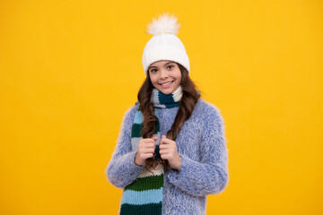 Beautiful teen girl in a winter hat and a warm sweater. A child on a yellow isolated background. Happy girl face, positive and smiling emotions.