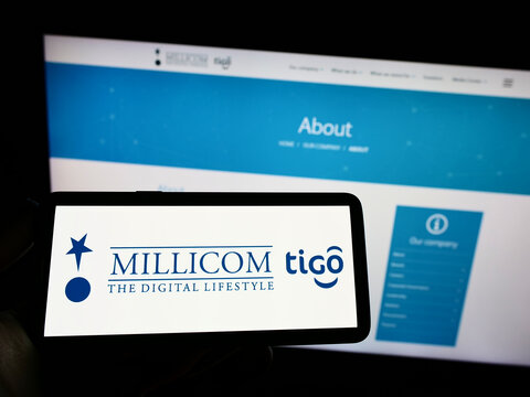 Stuttgart, Germany - 10-03-2022: Person holding cellphone with logo of company Millicom International Cellular S.A. on screen in front of business webpage. Focus on phone display.