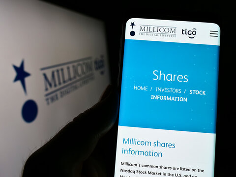 Stuttgart, Germany - 10-03-2022: Person holding cellphone with webpage of company Millicom International Cellular SA on screen in front of logo. Focus on center of phone display.