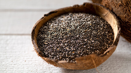 Chia seeds in a coconut bowl on a white wooden background, close-up