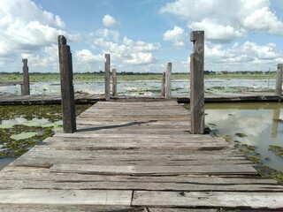 An old wooden bridge that spans a lake in the Thai countryside.