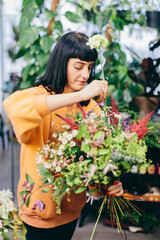 Woman arranges bouquet from flowers in florist shop
