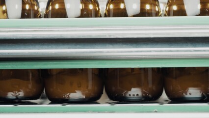 A row of glass bottles drive up and fill up with a liquid agent on a factory line. Manufacture drugs for medical supplies of pharmacy industry. Automatic bottling line. Close up