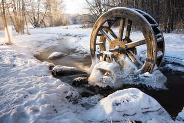 Frozen creek with water wheel in winter surrounded by trees