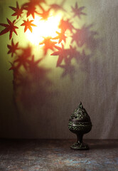 An ancient Chinese incense burner on a blurred night background of autumn maple leaves