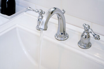 Bathroom shiny Stainless steel water mixer faucet or mixer tap in classic vintage style with water flowing out ,selective focus on the tip of faucet