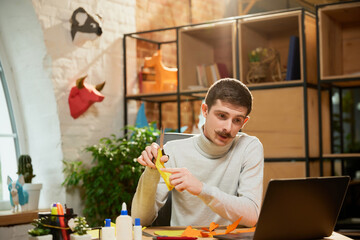 Young man sitting at home, holds a master class on origami and recording vlog at home studio. Hobbies and leisure activities. Remote training, online classes