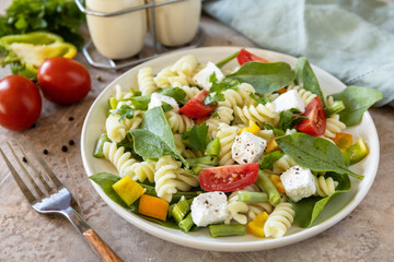 Salad with gluten free pasta, spinach, tomatoes, beans and feta cheese on a stone table. Italian food. Healthy food, vegetarian appetizer.
