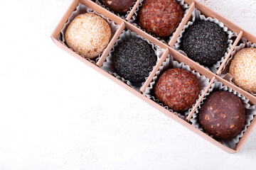 Assorted raw vegan sweets with nuts, seeds and dried fruit in cardboard box on white. Handmade sugar free candies. Top view