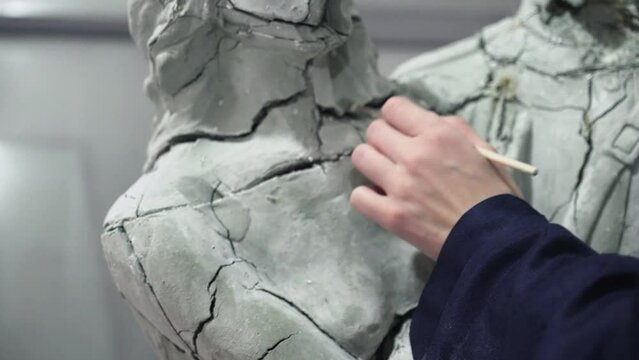 Close up od female sculptor uses brush to clean plaster sculpture of woman