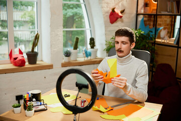 Making paper animal. Young man holds a master class on origami and recording vlog at home studio. Hobbies and leisure activities. Remote training, online classes