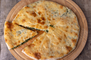 Pie with spinach, herbs and suluguni cheese on a wooden board. Whole pie with cut off piece....
