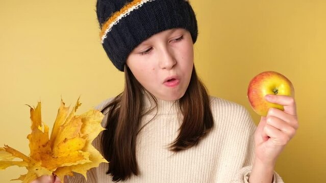 Teen Girl Eating an Apple Isolated on Yellow. Cute Young Girl in Knitted Cozy Clothes Biting Apples on Color Studio Background. Healthy Food Harvest. Autumnal Mood. Fall Season, Sale. Autumn Leaves.