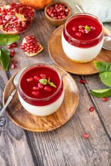 Winter delicious italian dessert panna cotta with pomegranate jelly and mint, homemade cuisine on a wooden background. Copy space.