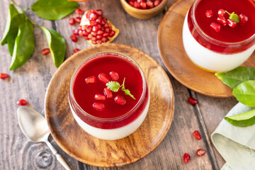 Winter delicious italian dessert panna cotta with pomegranate jelly and mint, homemade cuisine on a wooden background.