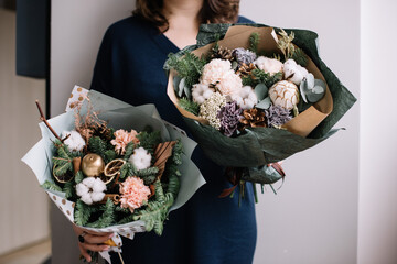 Very nice young woman holding two big and beautiful winter bouquets of fresh nobilis spruce, cotton, ornaments, carnations, cinnamon, eucalyptus flowers, cropped photo, bouquet close up