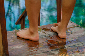Men's feet stand on the pier while relaxing on the shore of a tropical lake.