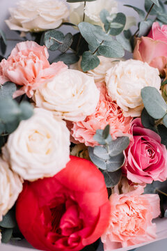 Very nice young woman holding big and beautiful bouquet of fresh peony, roses, eustoma, eucalyptus, carnations flowers in pastel pink and coral colors, cropped photo, bouquet close up