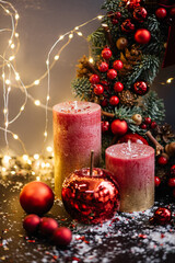 Beautiful festive arrangement: red candles, decorative apple, ornaments and a hand made winter wreath on the background with sparkling fireflies, vertical photo