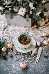 Beautiful festive winter set: pine cone in a cup, ornaments, beads, spruce branches, fake snow, glitter on the grey table background, close up view 