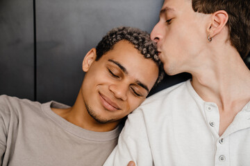 Happy young multiracial gay couple smiling and hugging together at home