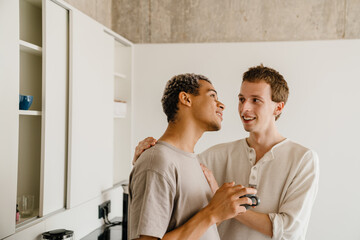 Obraz premium Happy young gay couple hugging while drinking coffee together at home