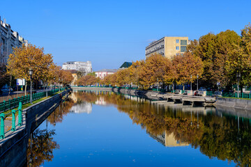 Fototapeta premium Landscape with Dambovita river, old buildings and yellow, orange and brown leaves in large trees in the center of Bucharest, Romania, in a sunny autumn day.