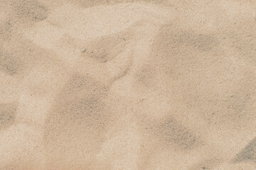 Close-up of a sandy beach. Background with sand unevenly swept away by wind and waves into small dunes. Background for a cover or design on the theme of travel.