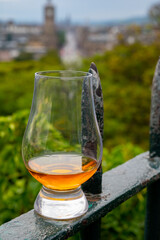 Glass of single malt scotch whisky and view from Calton hill to park and old parts of Edinburgh city in rainy day, Scotland, UK