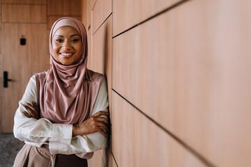 Happy muslim businesswoman standing by wall while working in office