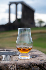 Glass of single malt scotch whisky and view from Calton hill to park and old parts of Edinburgh city in rainy day, Scotland, UK