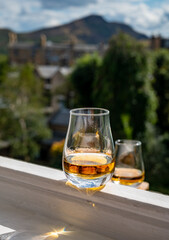 Glass of single malt scotch whisky served on old white window sill in Scottisch house with view on old part of Edinburgh and hills, Scotland, UK