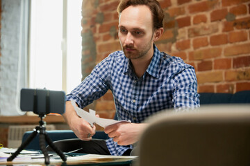 Young happy man holds a master class on appliques, quilling and recording vlog at home studio. Hobbies and leisure activities. Remote training, online classes