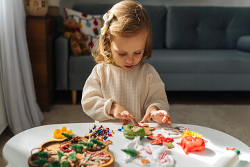 A little girl playing with play dough and Christmas decorations. Child hands creating Christmas crafts. Holiday Art Activity for Kids. Sensory play for toddlers.