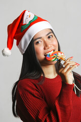 happy young beautiful asian woman wearing christmas hat and red sweater eating colorful lollipops