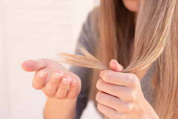 Close up view of unrecognizable woman holding damage hair with split ends with selective focus and blurred background