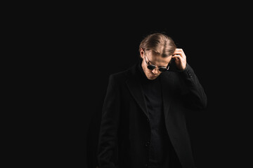Fototapeta premium stylish man in sunglasses and a black coat on a black background, a handsome and brutal man with long hair.