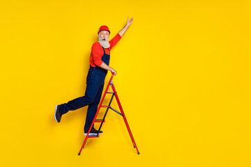 Full length photo of positive funky age man wear overall uniform red hard hat walking ladder empty space isolated yellow color background
