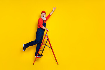 Full length photo of positive funky age man wear overall uniform red hard hat walking ladder empty...